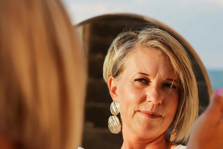 Woman examining reactive, dull-looking facial skin in the mirror as visible signs of aging appear more noticeable.